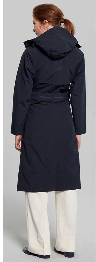Vrouw met lange donkerblauwe jas met capuchon, ceintuur en witte broek, van achteren gezien.