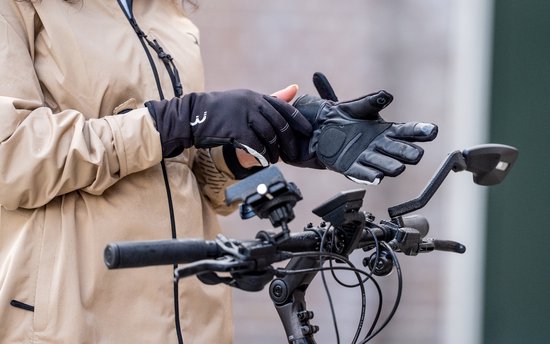 Vrouw trekt zwarte winterfietshandschoenen aan met witte accenten en een '3' logo, bij een fietsstuur.