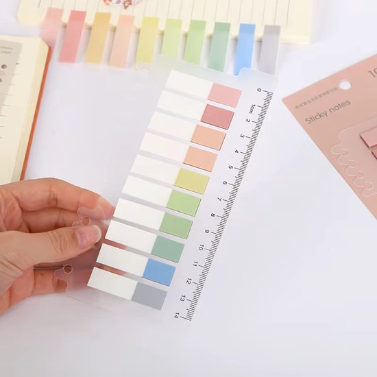 Hand houdt transparante sticky notes met liniaal vast, met pastelkleuren: roze, oranje, geel, groen, blauw en grijs.