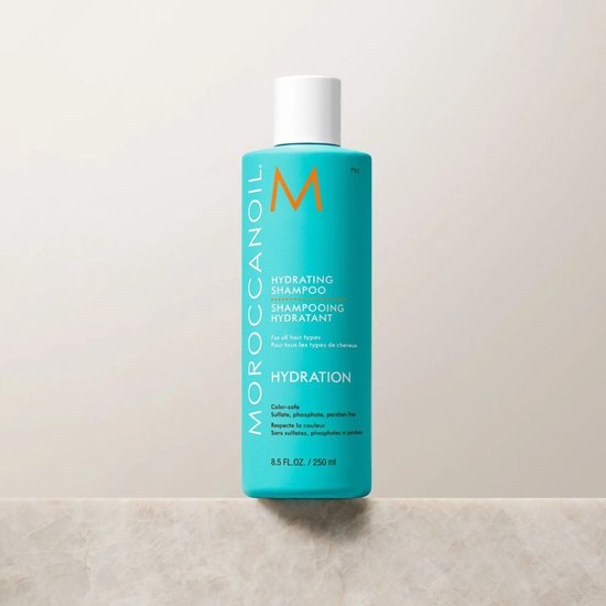 Hand houdt een turquoise Moroccanoil Hydrating Shampoo fles van 8.5 FL.OZ. / 250 ml vast.