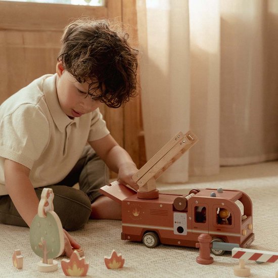 Kind speelt met houten brandweerwagen, ladder, poppetjes, boom, hydrant en vuurelementen.