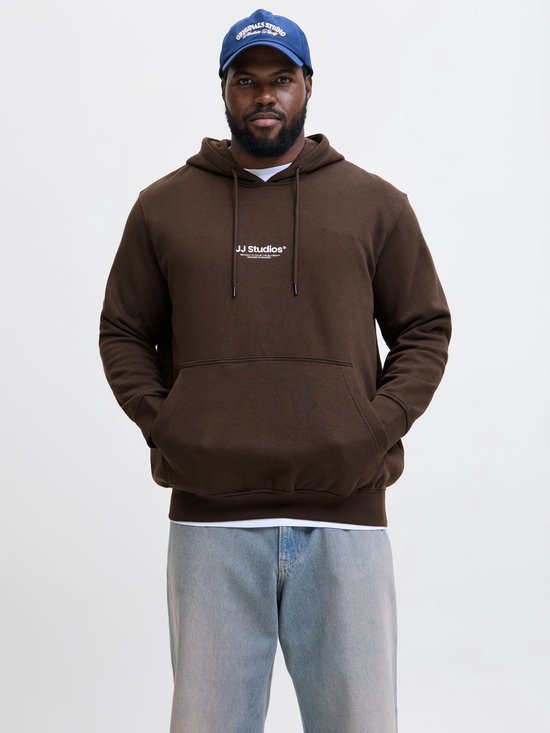Man met een blauwe pet en een bruine hoodie met 'JJ Studios' op de borst, gecombineerd met een lichte spijkerbroek.