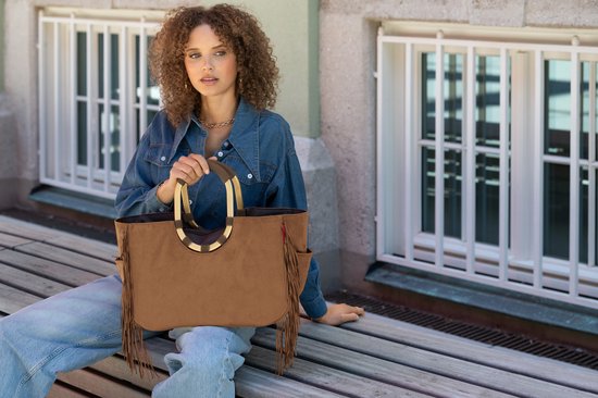 Model met bruine suède tas met franjes en gouden handvatten. Ze draagt een spijkerblouse en jeans.