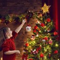 Meisje versiert kerstboom met gouden ster piek en rode kerstballen.