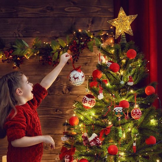 Meisje versiert kerstboom met gouden ster piek en rode kerstballen.