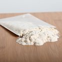 Zakje met lichte poederachtige substantie, half openliggend op een houten ondergrond.
