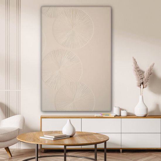 Beige canvas met drie reliëf cirkels, hangend boven een tv-meubel met boeken en een vaas met pampasgras.