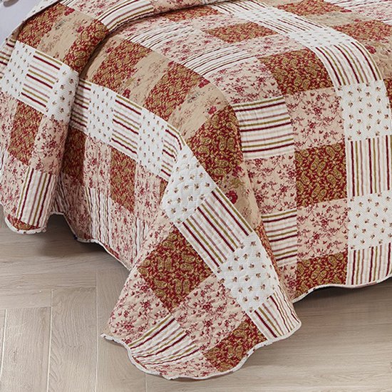 Bordeauxrode quilt met patchwork motieven, gedrapeerd over een bed. Bloemige, paisley en streepdessins.