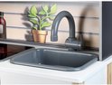 Grijze kraan boven een grijze gootsteen op de Miele speelgoedkeuken, met achtergrond van plant en houten lamellen.