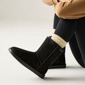 Damesbenen in zwarte legging met beige enkelsokken, zittend met zwarte laarzen.