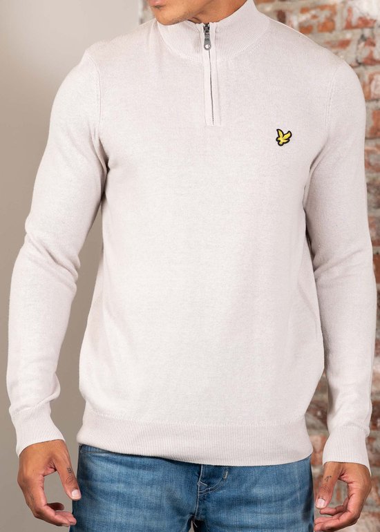 Man in licht beige gebreide trui met halve rits en jeans.