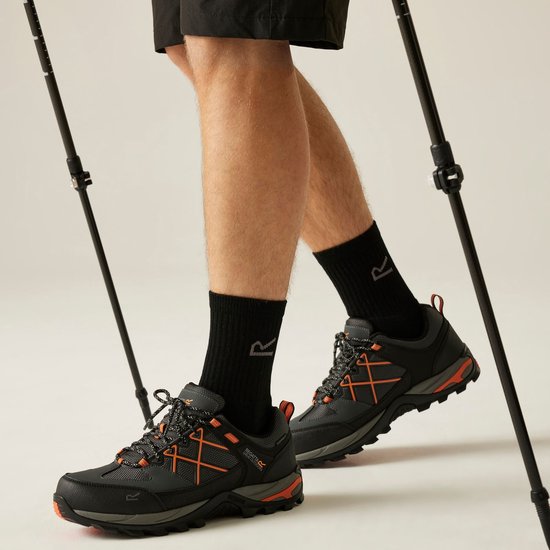 Man met zwarte sokken en oranje-zwarte Regatta wandelschoenen, staand met wandelstokken.