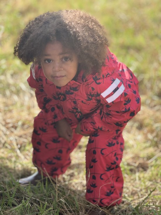 Kind in rood regenpak met donkerblauwe bloemenprint, gehurkt in gras.