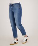 Zij-aanzicht van een model in een blauwe spijkerbroek met omgeslagen broekspijpen en sneakers.