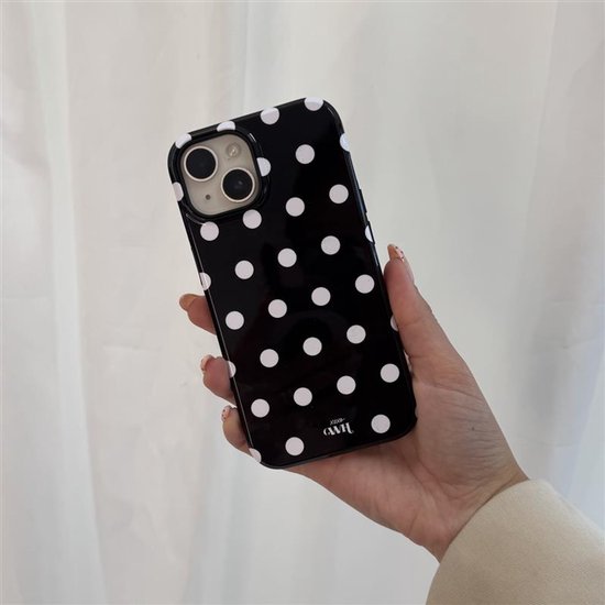 Een hand met een telefoonhoesje met witte stippen op zwarte achtergrond.