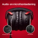 Close-up van zwarte gaming headset met rode details en audio/mic controls.