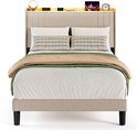 Een volledig opgemaakt beige gestoffeerd bed met kussens, plaids en een verlicht hoofdbord met opbergruimte.