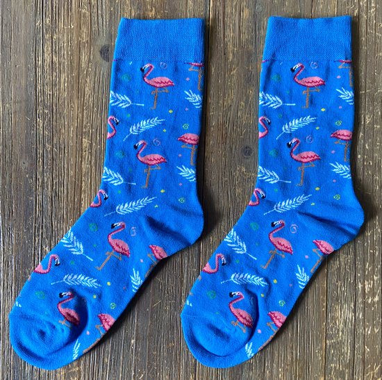 Blauwe sokken met een patroon van roze flamingo's, witte veren en gele stippen, op een houten achtergrond.