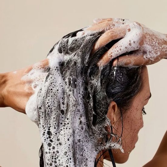 Femme se lavant les cheveux avec du shampoing moussant Gingembre The Body Shop. Traitement pour cuir chevelu squameux.