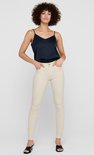 Model in crème skinny jeans met zwarte top met spaghettibandjes en sandalen.