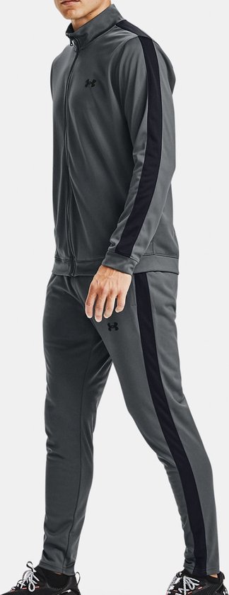 Man in profiel met een grijs Under Armour trainingspak. Zwarte strepen op de mouwen en zijkanten van de broek.