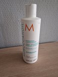 Witte Moroccanoil Hydrating Conditioner fles met oranje M-logo op een houten ondergrond.