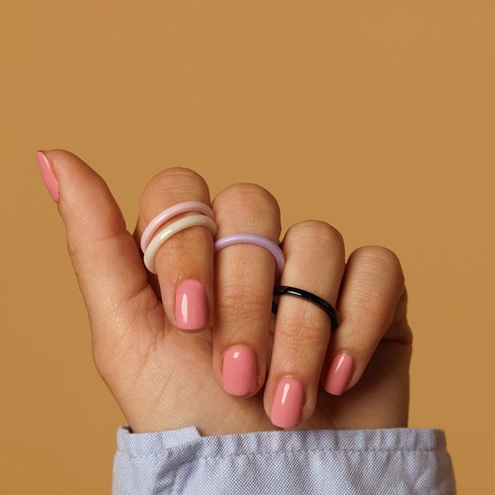 Hand met roze nagellak draagt vier smalle ringen: twee lila, een witte en een zwarte.