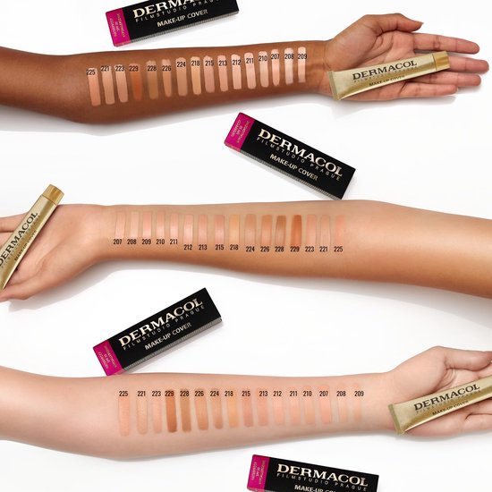 Drie armen met verschillende huidtinten, waarop foundation is aangebracht. Gouden tubes en zwarte verpakkingen van "DERMACOL" zijn zichtbaar.