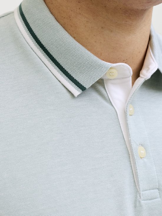 Close-up van de kraag van een lichtgroen poloshirt met witte knopen en groene en witte streepjes.