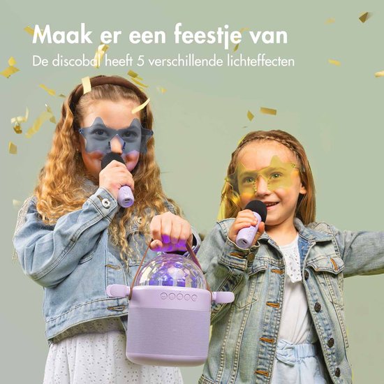 Twee meisjes met spijkerjasjes en gekleurde sterrenbrillen zingen enthousiast in microfoons, omringd door confetti. De karaokespeaker met discobal is in hun handen.