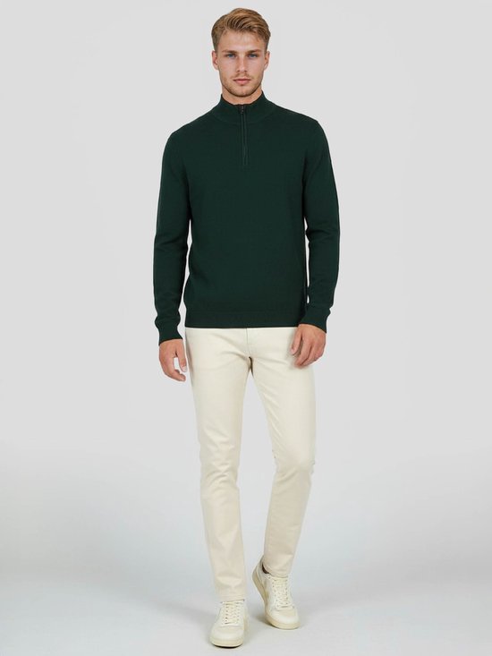 Homme portant un pull en laine mérinos vert foncé avec fermeture éclair à la gorge, associé à un chino crème.