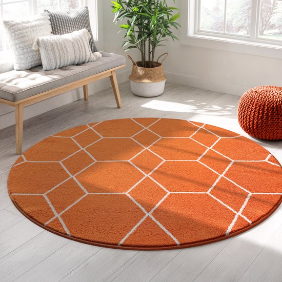 Oranje rond vloerkleed met wit geometrisch patroon in een woonkamer met een grijze bank en oranje poef.