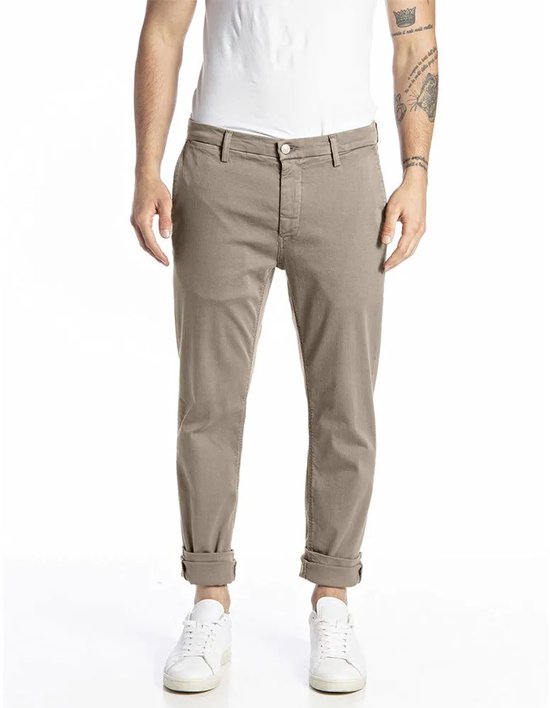 Mannelijke chino in beige met opgerolde broekspijpen en witte sneakers.