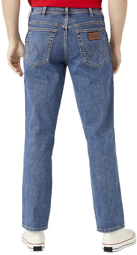 Achterkant van een blauwe spijkerbroek met bruin label en witte sneakers.