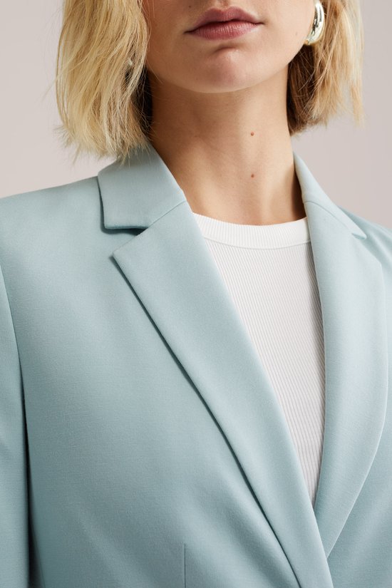 Close-up van een lichtblauwe blazer met open kraag, gedragen over een witte top.