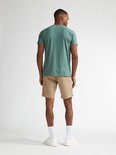 Man van achteren gezien in een beige chino short met een groene t-shirt, witte sokken en sneakers.