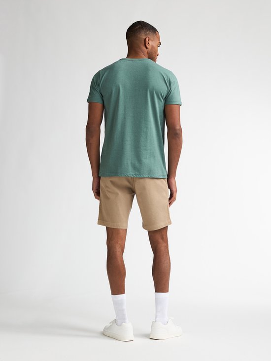 Man van achteren gezien in een beige chino short met een groene t-shirt, witte sokken en sneakers.