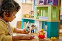 Enfant jouant avec une maison Duplo, avec des figurines Duplo et un chariot.