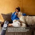 Vrouw knuffelt hond op bank, met afstandsbediening; past licht en ventilator aan.