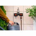 Gardena waterverdeler met twee oranje knoppen. Een slang is aangesloten, de ander vult een grijze gieter.