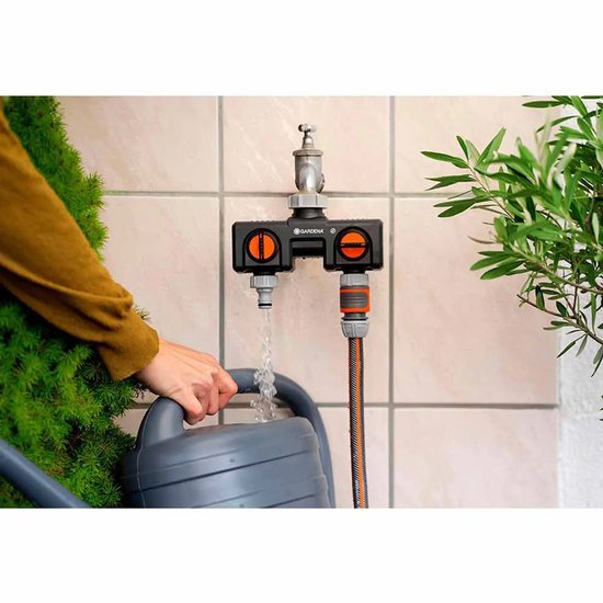 Gardena waterverdeler met twee oranje knoppen. Een slang is aangesloten, de ander vult een grijze gieter.