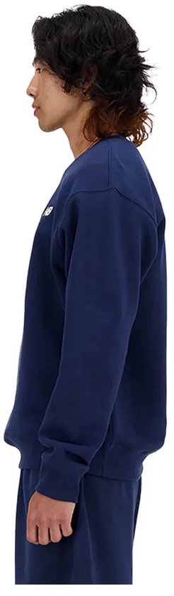 Man van de zijkant, draagt donkerblauwe New Balance trui met wit logo.