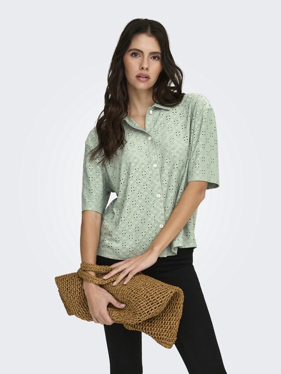 Model met lichtgroene blouse met korte mouwen, broderie anglaise en bruine tas.