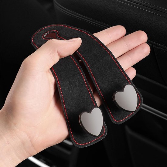 Een hand houdt twee zwarte autohaken met rode stiksels en hartvormige zilveren details vast.