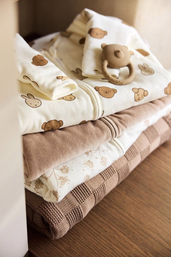 Stapel beige slaapzakken en dekens met prints van beren, konijnen en bloemen. Een bijtring met beer ligt erop.