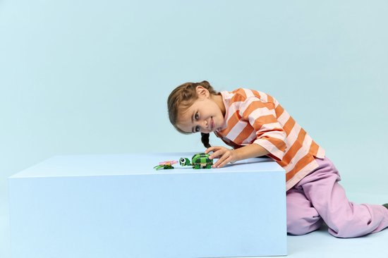 Meisje met oranje gestreepte trui en roze broek speelt met groene LEGO-schildpad en waterlelie.