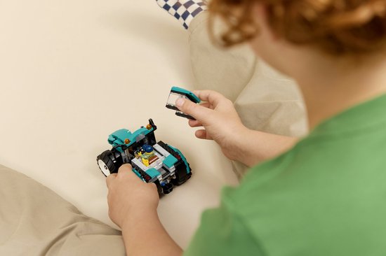 Jongen met blauwe pet bouwt aan een felgroene tractor met losse onderdelen.