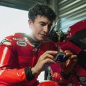 Marc Márquez in rood racepak kijkt naar een Insta360 actiecamera in zijn handen.
