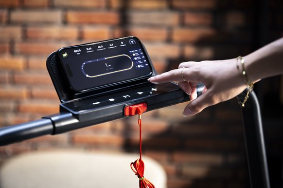 Close-up van een smartphone op de houder van de AJ-Sports loopband, met een vinger die het scherm aanraakt.