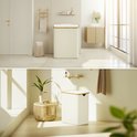 Crèmekleurige wasmand met bamboe rand, in een lichte badkamer en slaapkamer.